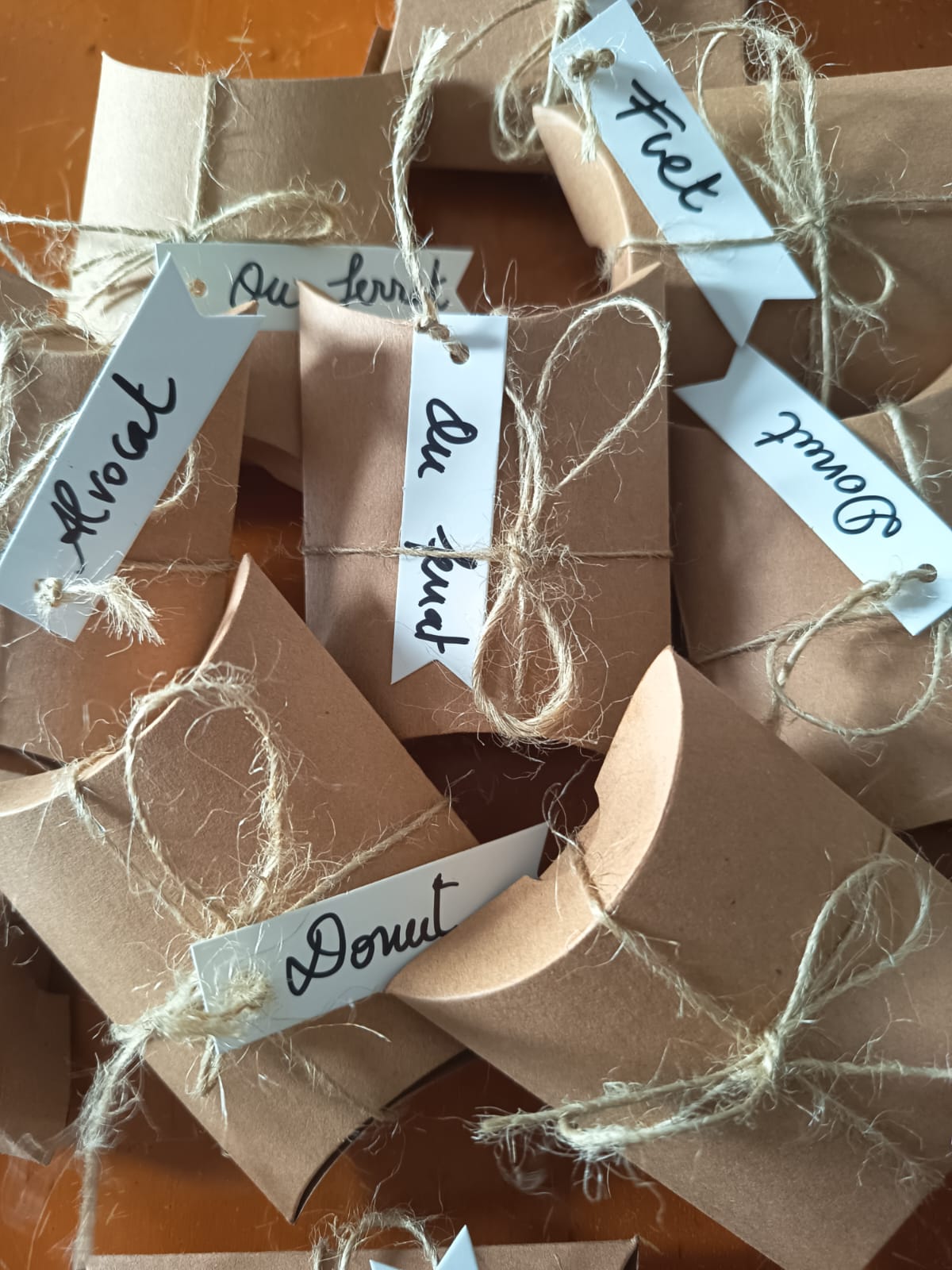 Paquets de cartró kraft lligats amb cordill, cadascun amb una etiqueta manuscrita: fuet, dònut, ou ferrat, alvocat.